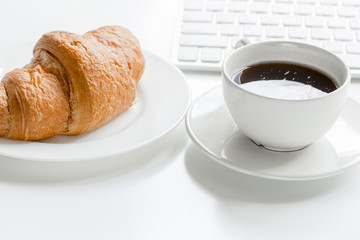Business breakfast in office with keyboard, coffee and croissant on white table background