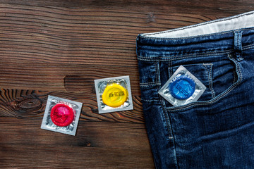 condoms and jeans for male contraception and birth control wooden background top view