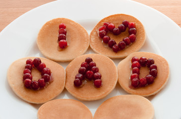 Pancakes with cranberries and syrup on a white plate on a wooden background. Happy Father's Day. Breakfast. Surprise. I love Dad.