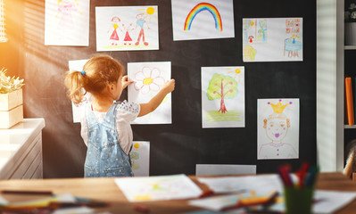 child girl hanging her drawings on wall.