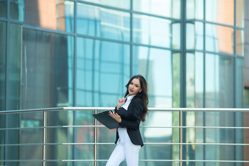 Beautiful young girl in a suit with a black folder in hands on the background of a glass building