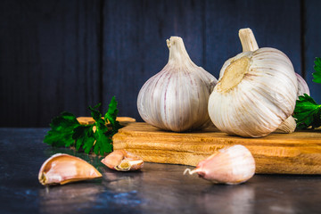 Garlic cloves and garlic bulb on a wooden board on a gray background.