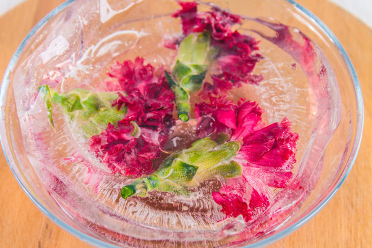 Carnation flowers in ice, on a wooden background