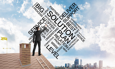Young businessman standing on house roof and writing leadership skill concept. Mixed media