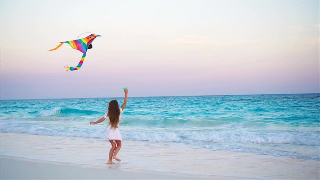 Little girl with flying kite on tropical beach. Kid play on ocean shore. Child with beach toys in slow motion