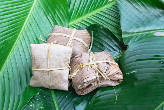 Close-up group of traditional cakes from the North of Vietnam wrapped on dried banana leaves tie with rice straw on large green leaves called la dong (Phrynium placentarium).Sweet rice cake (banh gai)