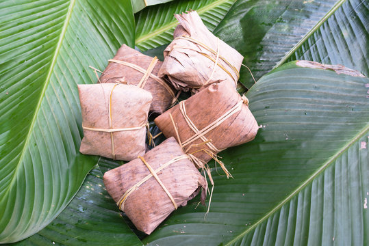 Close-up group of traditional cakes from the North of Vietnam wrapped on dried banana leaves tie with rice straw on large green leaves called la dong (Phrynium placentarium).Sweet rice cake (banh gai)