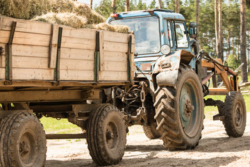 Tractor carries a trailer with bales of hay.