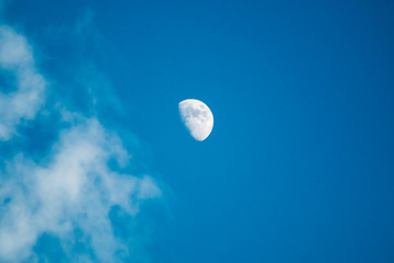 Moon and clouds in the deep blue sky during the day.