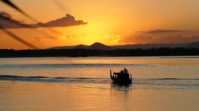 Silhouette of a gondola boat passing by a sunset over mountains.