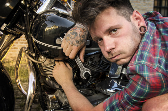 Exhausted man with wrench working on motorbike, funny face, selective focus on hand with wrench. Man having trouble with motorcycle 