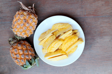 Cutting fresh pineapple and pineapple shelled Asian-style in white dish on the old wooden background. Tropical fruit concept.