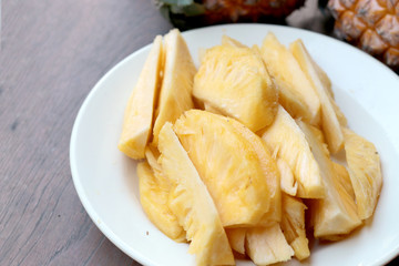 Cutting fresh pineapple and pineapple shelled Asian-style in white dish on the old wooden background. Tropical fruit concept.