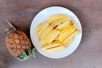 Cutting fresh pineapple and pineapple shelled Asian-style in white dish on the old wooden background. Tropical fruit concept.