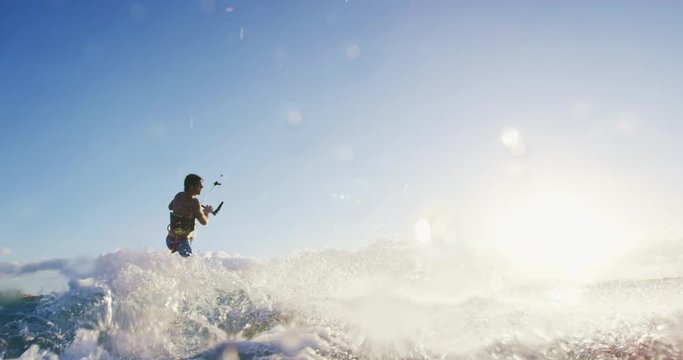 Young man kitesurfing on surfboard in blue ocean at sunet