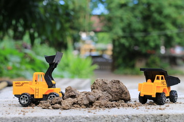 Truck toy car with sand and soil on the concrete floor with blur boken green environment  construction equipment at work ,construction concept, selective focus.