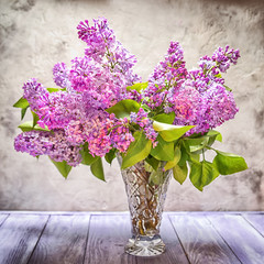 A bouquet of lilac in a crystal vase on the background of a textured wall