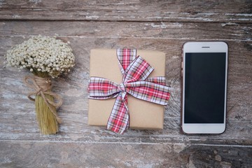 Bouquet flowers, gift box and phone on vintage and old wooden table.