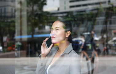 business woman using a smartphone at reflection glass of office building.