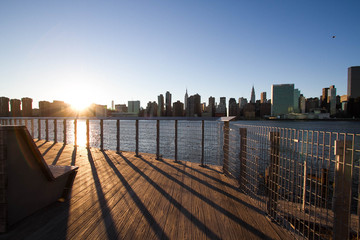 Wooden walkway and fence at Gantry Plaza State Park next to East river and Manhattan with sunset © Spinel