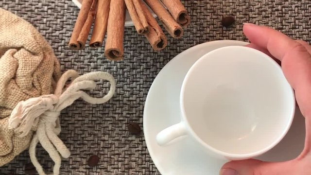 Coffee. A white cup is put on the table, poured hot black with foam, bubbles of aroma steam. Close-up of coffee beans table, cinnamon sticks, spoon texture of burlap sack. HD video