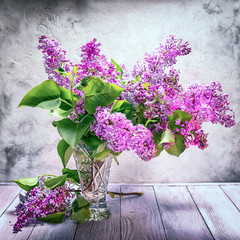Still life bouquet of lilac in a crystal vase on the background of a textured wall