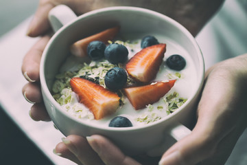 Woman hands holding bowl with tasty muesli with fruits, oat and yogurt. Closeup. Healthy Food Concept. Toning.