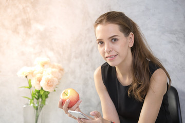Beautiful young woman using smartphone while eating apple, 20s year old.