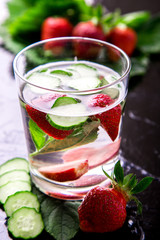 Cucumber and strawberry detox water in glass on black background. Backlight. Diet.