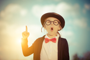 Funny little girl in glasses, bow tie and bowler hat pointing finger up. Retro stile.