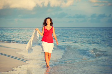 Fototapeta na wymiar Attractive young woman walking along ocean beach at sunset