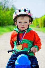 Fototapeta na wymiar Toddler on pushbike with medal as a confident winner of a race. Child concept.