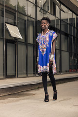 one, young adult, black african american woman, 20-29 years, smiling walking pavement, building exterior, looking to camera, outdoors, wearing blue dress, tights, high heel shoes, fashionable