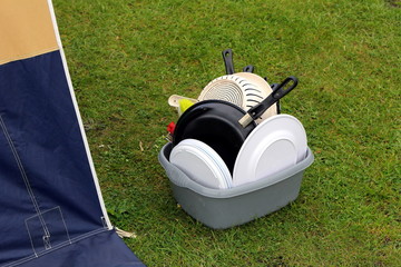 Washing up bowl with dirty pots and plates, on the grass outside a tent at a camp site