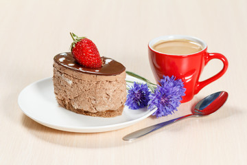 Chocolate cake on the white plate with cornflowers and a cup of coffee