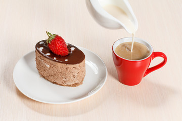 Chocolate cake on the white plate with a cup of coffee and a gravy boat with milk