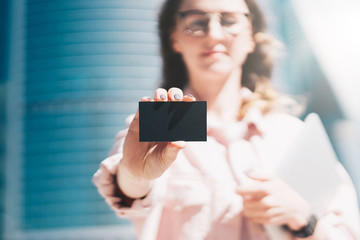 Close-up of black empty credit, business, calling, visiting card in hand of young businesswoman, standing outdoors.