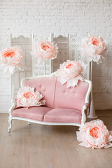 Soft sofa with pretty pink fabric upholstery in a room with wooden floor and white walls. And big paper flowers around it