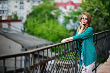 Trendy girl at glasses and ripped jeans against barrier on street.