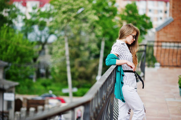 Trendy girl at glasses and ripped jeans against barrier on street.