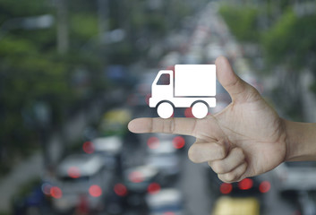 Truck delivery icon on finger over blur of rush hour with cars and road, Transportation business concept