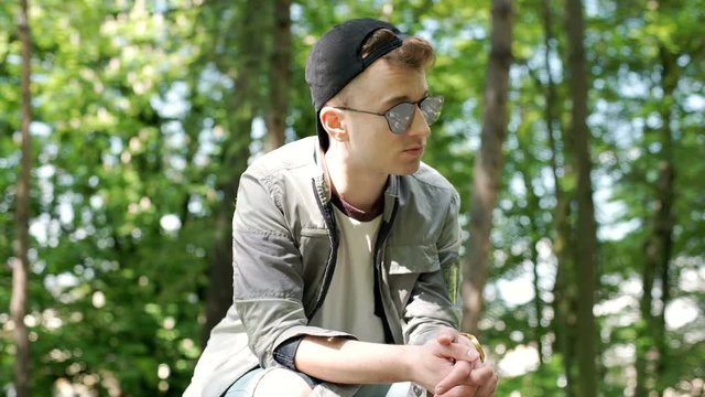 Young man looks stylish while relaxing in the park, steadycam shot
