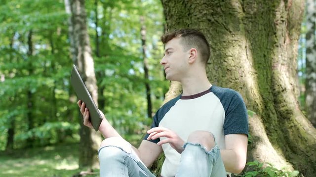 Boy looks dissatisfied while doing photos on tablet in the park, steadycam shot
