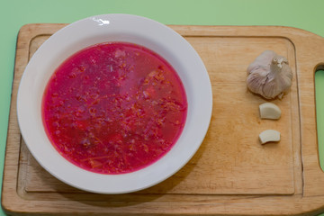Borscht in a white plate and next to garlic. National Russian Food