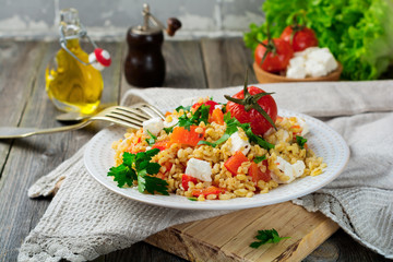 Tabula. Bulgur with baked pepper, tomato and feta cheese on an old wooden background. Selective focus.