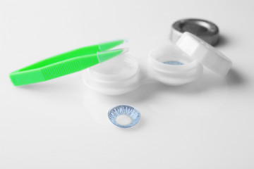 Container with blue contact lenses and tweezers on white background