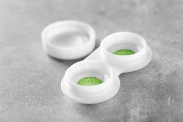 Container with green contact lenses on grey table