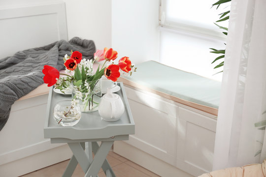 Vase with beautiful flowers and tea set on table in modern veranda interior
