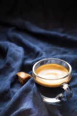 Cup of espresso against dark background with a chunk of cantucci biscuit