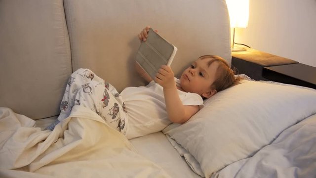 4k footage of adorable baby boy lying in bed and holding digital tablet